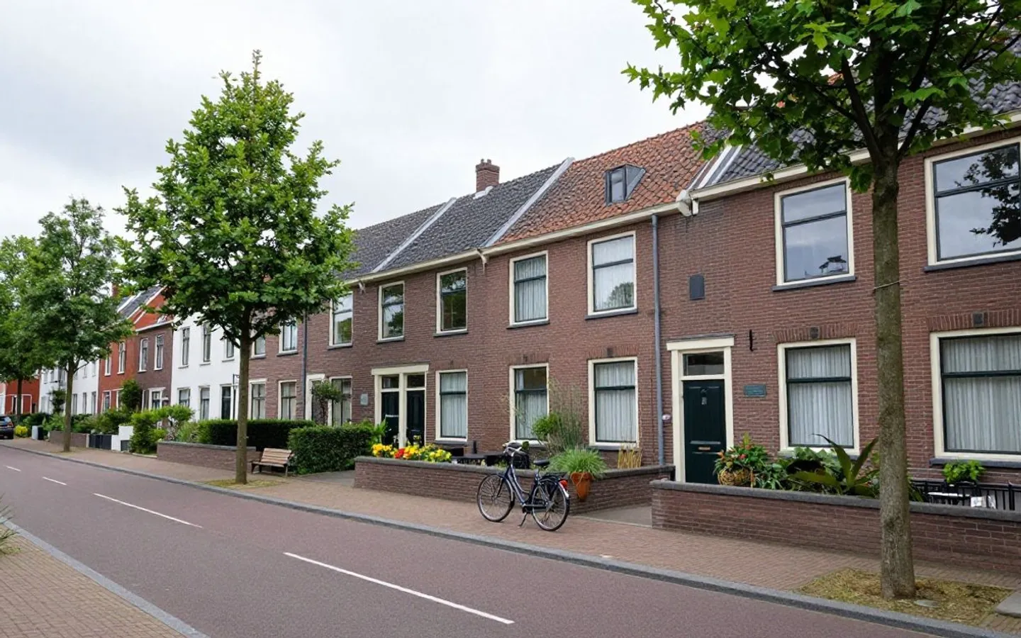Een lange rij rijwoningen met voortuintjes aan een rustige straat.
